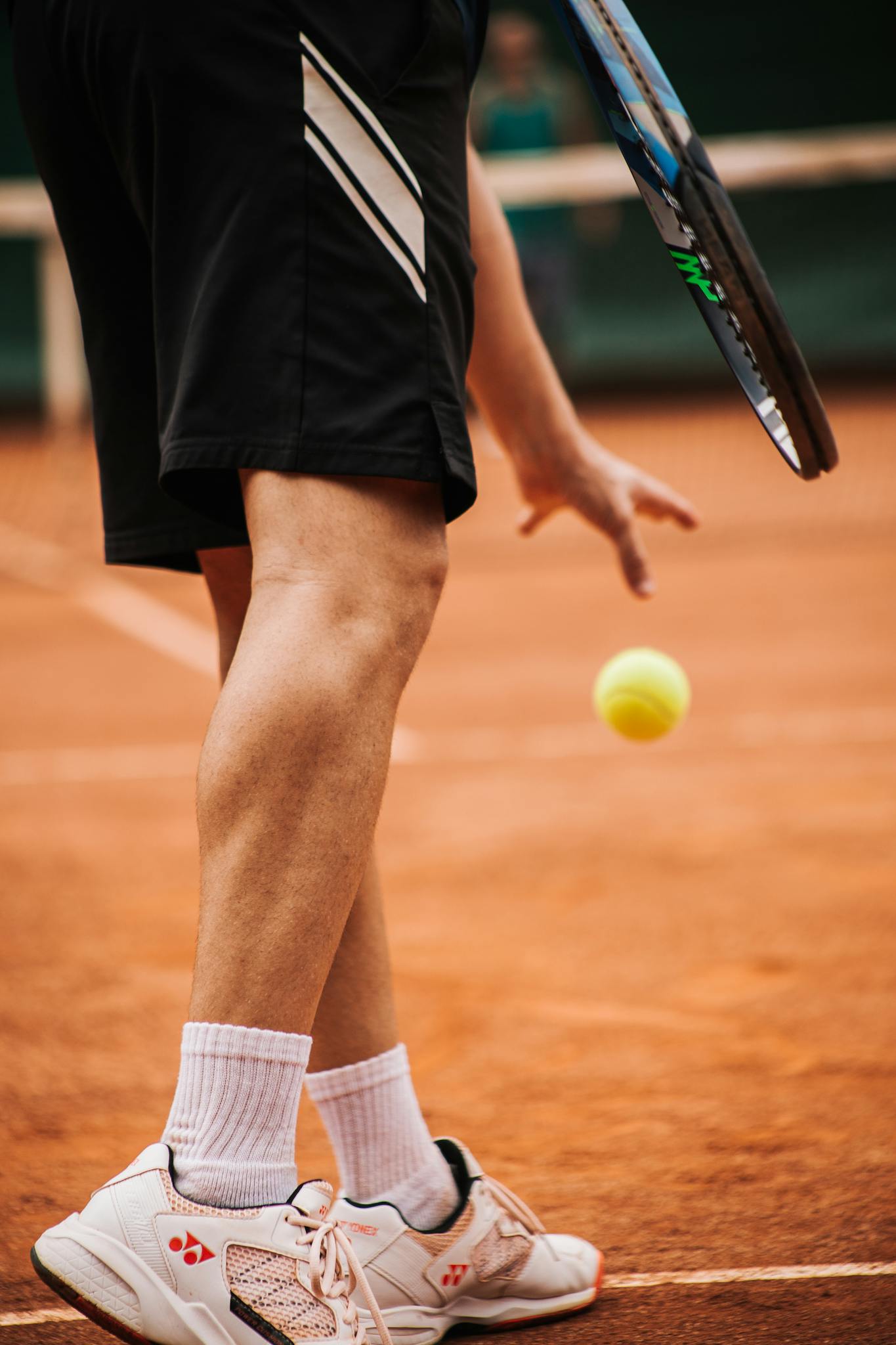 Close-up of male tennis player bouncing ball on clay court with racket.